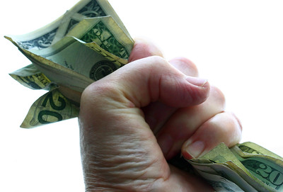 La imagen es una fotografía de una mano apretando fuertemente algunos billetes, en expresión de codicia.